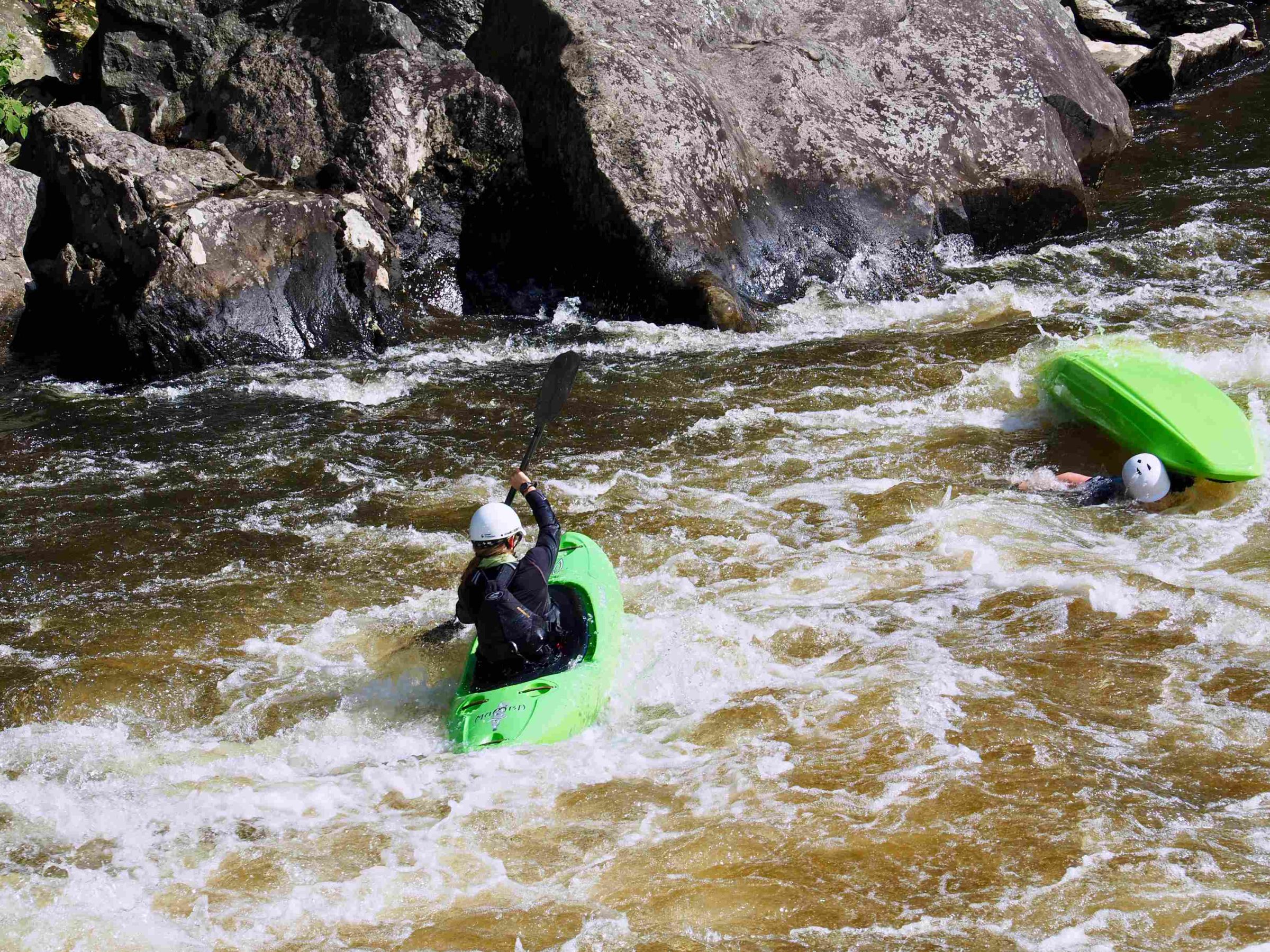 two kayakers in white water with one boat flipped upside down